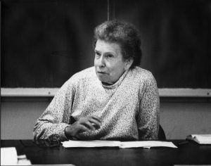 Prof. Mabel Lang teaching, seated at a desk in front of a blackboard.